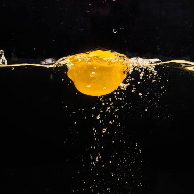 Taze sarı limon suya dökülüyor, biraz su ve hava kabarcıklarıyla, siyah arka planda izole edilmiş..
