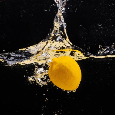 Taze sarı limon suya dökülüyor, biraz su ve hava kabarcıklarıyla, siyah arka planda izole edilmiş..