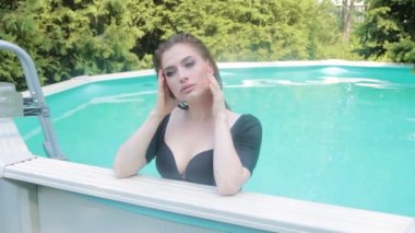 Havuzun kenarında suyun içinde dikilirken siyah mayo giymiş genç ve güzel bir kadının portresi. Sıcak yaz havasında suda dinlenmek.
