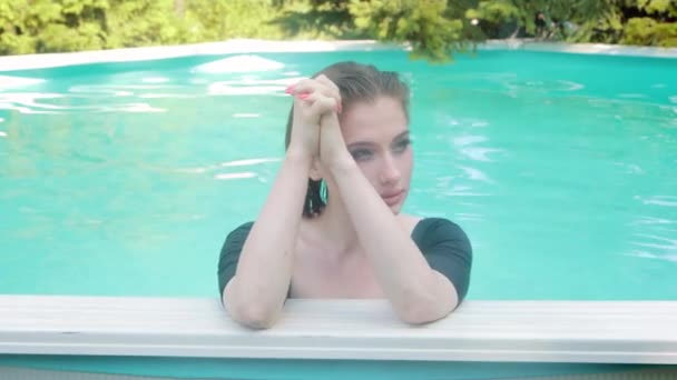 一个身穿黑色泳衣的年轻漂亮女人站在游泳池边的水里摆姿势的画像 炎热的夏天在水里放松一下 — 图库视频影像