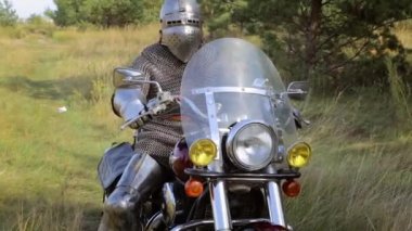 Zırhı, zırhı, zırhı ve kaskı olan bir ortaçağ savaşçısı motosikletten kalkar. Orta Çağ Şövalyesi modern bir bisiklette.