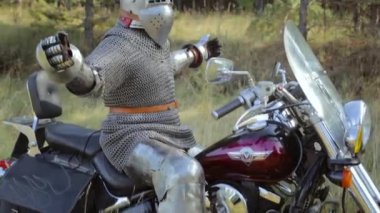 Zırhlı bir ortaçağ şövalyesi ormanın arka planında motosikletin üstünde oturur..
