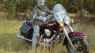 Zırhlı bir ortaçağ şövalyesi ormanın arka planında motosikletin üstünde oturur..
