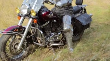 Zırhlı bir ortaçağ şövalyesi ormanın arka planında motosikletin üstünde oturur..