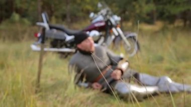 Ortaçağ zırhı giymiş bir şövalyeye seçici bir odak noktası ve bir bandana içinde bir motosiklet ve ormanın arka planına karşı çimlerin üzerinde yatıyor..