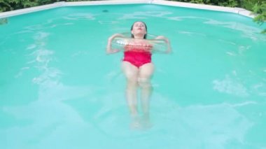 Kırmızı mayo giymiş genç çekici bir kadın lastik bir yüzükle sırt üstü havuzda yüzüyor. Sıcak yaz havasında suda dinlenmek.