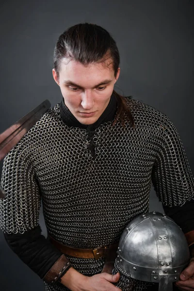 A medieval warrior in chain mail sits on his knee with a helmet in his hands. Knighting.