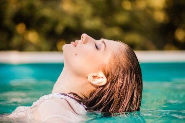 Havuzda göğsüne kadar duran beyaz gömlekli, ıslak saçlı güzel bir kızın portresi..