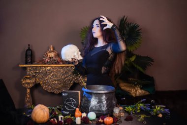 Elinde kafatası olan bir cadının portresi bir kazanın yanında duruyor ve içinde büyücülük için bitkiler ve malzemelerle dolu bir masa..