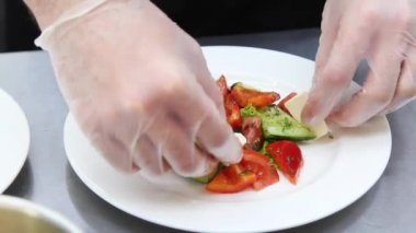 Aşçının elleri yakın plan bir tabağın üzerine doğranmış sebzeleri serer. Salata hazırlama süreci.