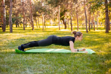 Genç bir kadın dirseklerinin üzerinde durarak karın kaslarını güçlendirmek için egzersiz yapar. Parkta spor eğitimi..