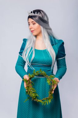 Bir prenses portresi, ortaçağ, fantezi, turkuaz elbise kül saçlı ve gümüş taç, elinde eğreltiotu dalları ile poz, beyaz bir arka plan izole.