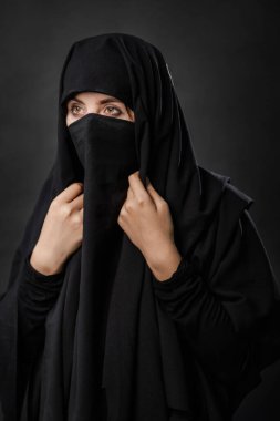 Siyah bir arka planda gizli bir yüzü olan siyah çarşaflı genç ve yetişkin bir kadının portresi..