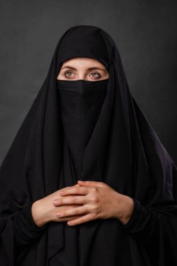 Siyah bir arka planda gizli bir yüzü olan siyah çarşaflı genç ve yetişkin bir kadının portresi..