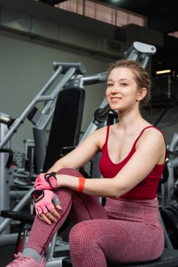 Spor salonundaki egzersiz makinesinde egzersiz makinelerinin arka planında poz veren genç atletik çekici kadın..