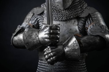 Ortaçağ şövalyelerinin zırhı, çelik ellerin kılıç tutuşu, karanlık arka planda izole edilmiş..