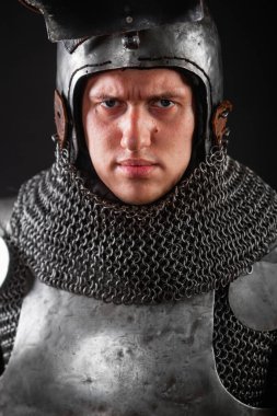 Kapsamlı zırhlı ve kasklı koyu renk arka planda vizörlü bir ortaçağ şövalyesi portresi..