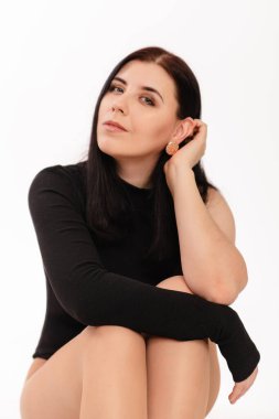 Siyah elbiseli genç bir kadın beyaz arka planda izole bir şekilde oturuyor..
