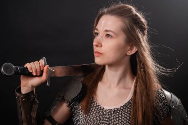 Genç bir kadının portresi, zırhlı fantezi savaşçısı elinde kılıçla karanlık bir arka planda..