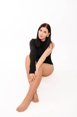 Siyah elbiseli genç bir kadın beyaz arka planda izole bir şekilde oturuyor..