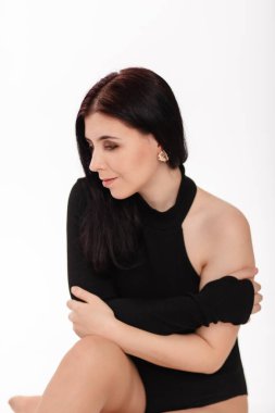 Siyah elbiseli genç bir kadın beyaz arka planda izole bir şekilde oturuyor..