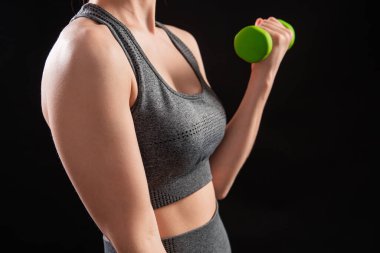 Dambılları tutan bir kadının yakın çekimi. Gri spor giyimli genç bir kadın stüdyoda siyah bir arkaplanda izole bir şekilde poz veriyor. Spor konsepti.