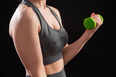 Dambılları tutan bir kadının yakın çekimi. Gri spor giyimli genç bir kadın stüdyoda siyah bir arkaplanda izole bir şekilde poz veriyor. Spor konsepti.