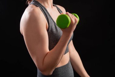 Dambılları tutan bir kadının yakın çekimi. Gri spor giyimli genç bir kadın stüdyoda siyah bir arkaplanda izole bir şekilde poz veriyor. Spor konsepti.