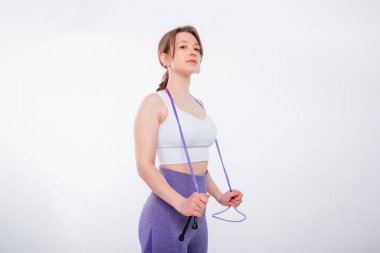 Spor kıyafetli genç bir kadının portresi. Elinde ip vardı. Stüdyoda beyaz bir arkaplanda izole bir şekilde poz veriyordu..