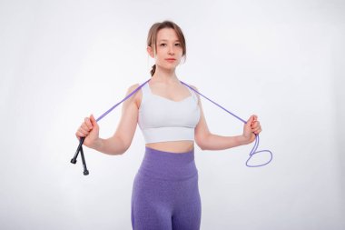 Spor kıyafetli genç bir kadının portresi. Elinde ip vardı. Stüdyoda beyaz bir arkaplanda izole bir şekilde poz veriyordu..