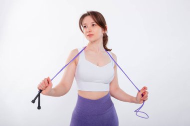 Spor kıyafetli genç bir kadının portresi. Elinde ip vardı. Stüdyoda beyaz bir arkaplanda izole bir şekilde poz veriyordu..