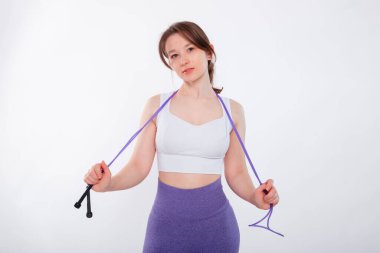 Spor kıyafetli genç bir kadının portresi. Elinde ip vardı. Stüdyoda beyaz bir arkaplanda izole bir şekilde poz veriyordu..