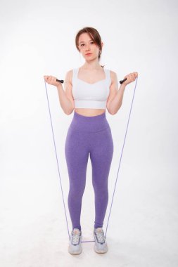 Spor kıyafetli genç bir kadının portresi. Elinde ip vardı. Stüdyoda beyaz bir arkaplanda izole bir şekilde poz veriyordu..
