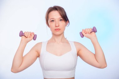 Spor kıyafetli genç bir bayan, beyaz arka planda izole haldeki halterleriyle poz veriyor..