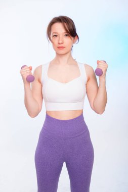 Spor kıyafetli genç bir bayan, beyaz arka planda izole haldeki halterleriyle poz veriyor..