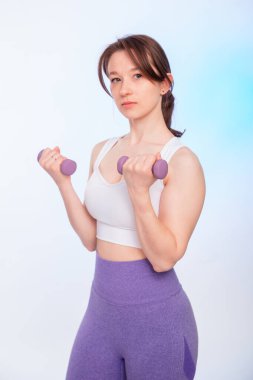 Spor kıyafetli genç bir bayan, beyaz arka planda izole haldeki halterleriyle poz veriyor..