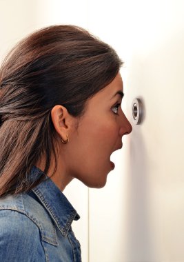Woman looking out through peephole clipart