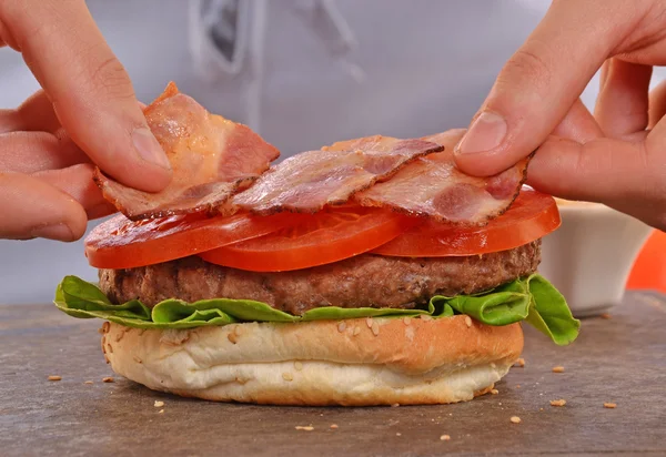 Cook adding tomato on hamburger — Stockfoto