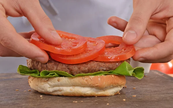 Cook adding tomato on hamburger — ストック写真