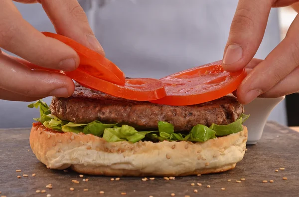 Cook adding tomato on hamburger — Stock Photo, Image