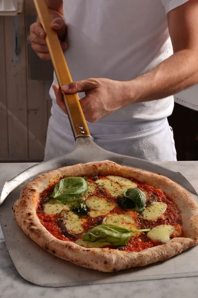 Cook taking out baked pizza