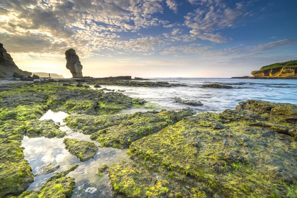 Rock green moss with sunrise background at Pantai Batu Payung ( Umbrella Rock Beach) lombok, Indonesia.