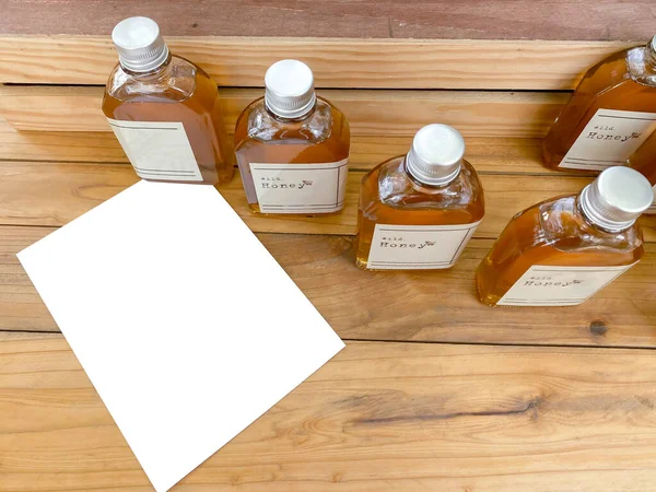 A little bottle of honey to make a souvenir and a mock up white card is placed on a wooden table.