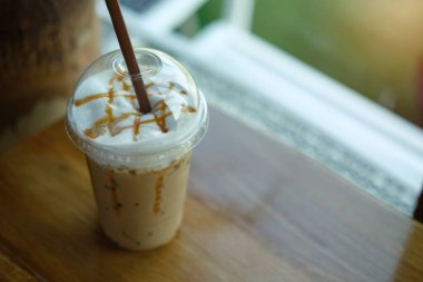 Kahve dükkanındaki ahşap bir masanın zeminine monte edilmiş plastik bardakta kapuçino kahvesi..