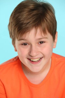 Yakın plan portre: turuncu tişörtlü yakışıklı ve neşeli bir çocuk gözyaşlarına gülüyor ve göz göze bakıyor..