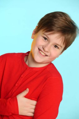 Yakın plan portre: son moda, kırmızı kazaklı neşeli genç çocuk. Gülümsüyor ve göz göze geliyor..