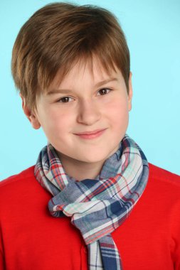 Yakın plan portre: Kırmızı süveter ve kareli atkı giyen şık, neşeli genç çocuk. Gülümser ve göz göze gelir..