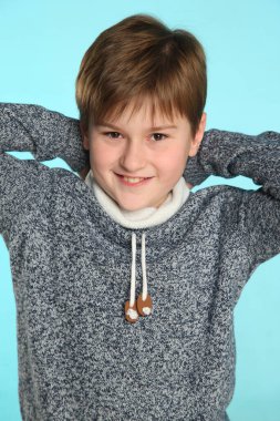 Yakışıklı, şık, neşeli genç çocuk ellerini başının arkasında tutuyor, gözlerinin içine bakıyor ve mutlu bir şekilde gülümsüyor..