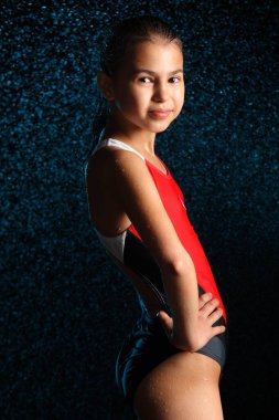 Siyah arka planda tek parça kırmızı mayo giyen ince ve güzel 12 yaşında bir kızın diz altı portresi, yan yana durur ve göze bakar..