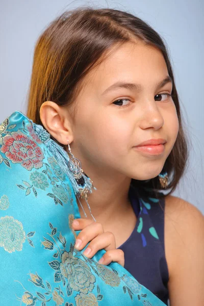 明るいかわいい黒髪の10代の少女のクローズアップポートレート12歳ダークブルーのドレスで 彼女は楽しそうに青い絹の枕の後ろからのぞき見 — ストック写真